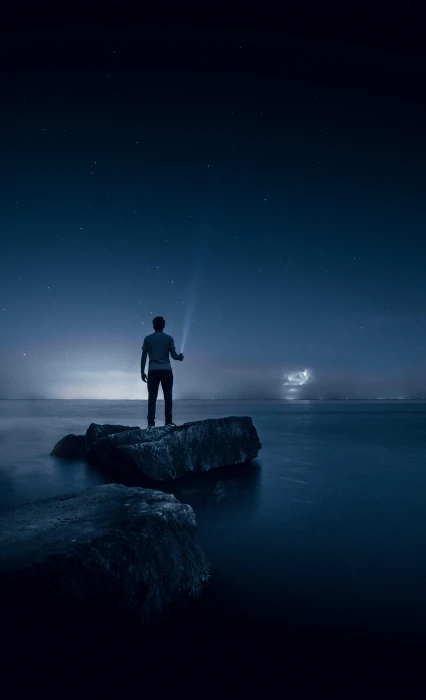 man holding flashlight standing on rock in white between body of water during night time 2k 4k
