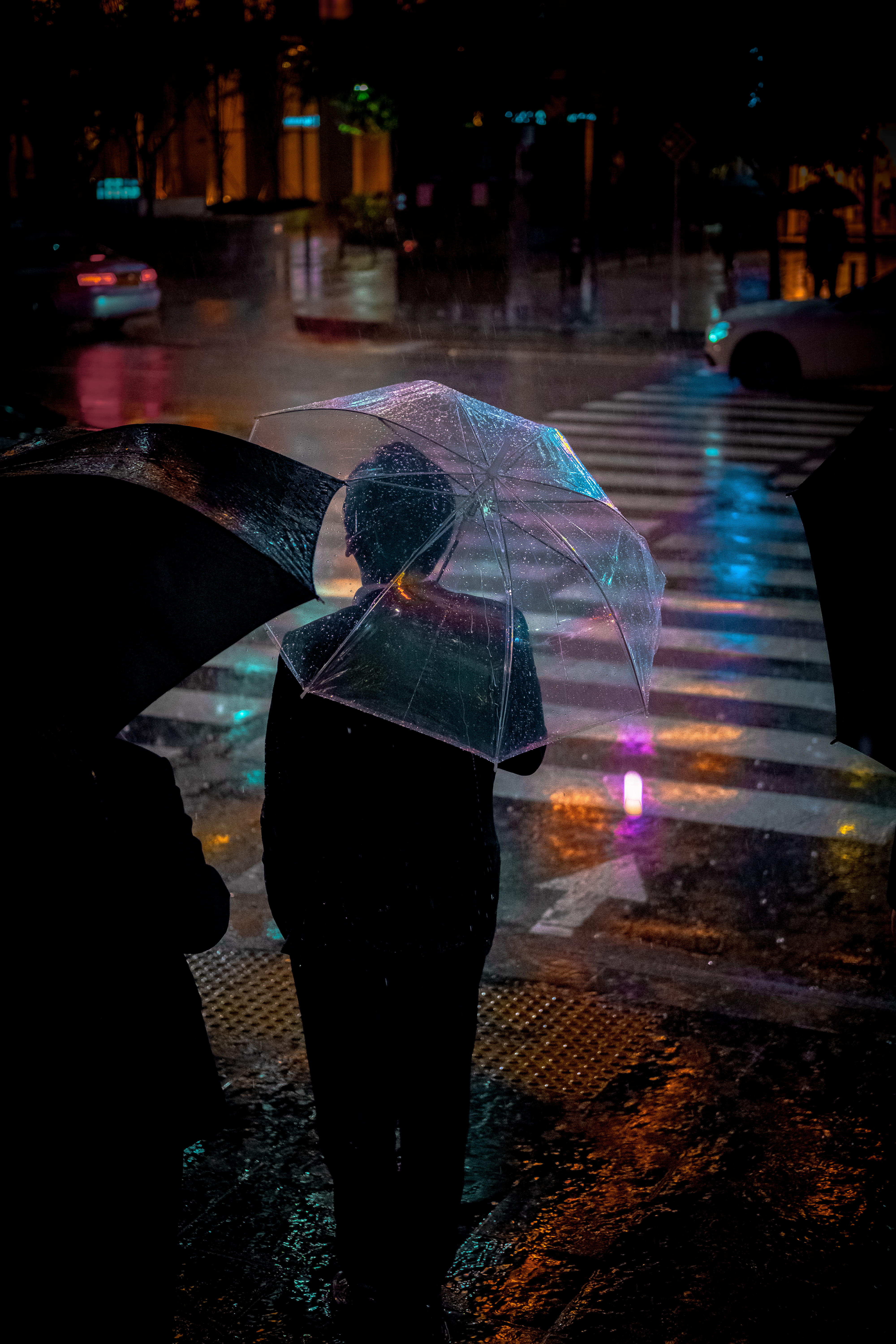 man wearing black suit jacket holding clear umbrella in front of pedestrian lane person standing near while carrying an during night 2k 4k