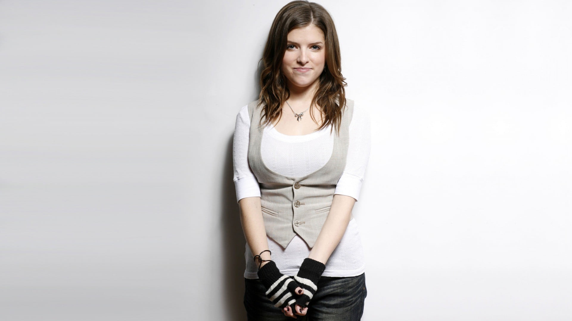 woman wears gray 3 button vest stands behind white painted wall