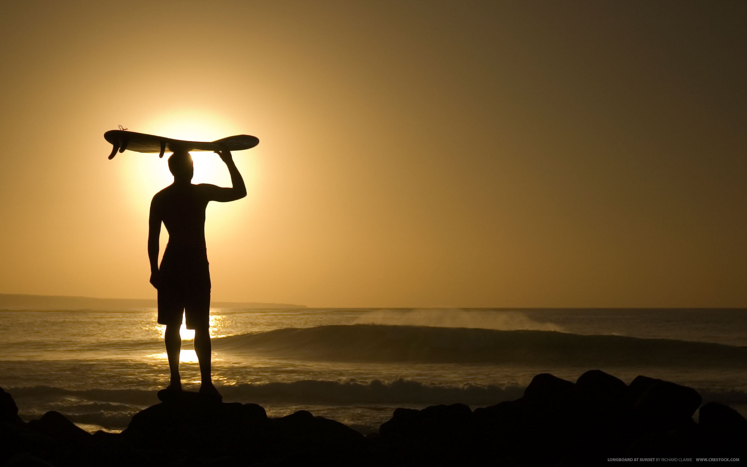 silhouette of man standing on rock beside beach during golden hour time 2k