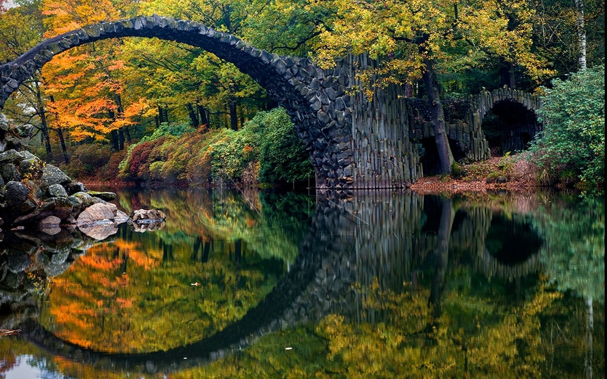 black concrete arch bridge body of water surrounded by trees