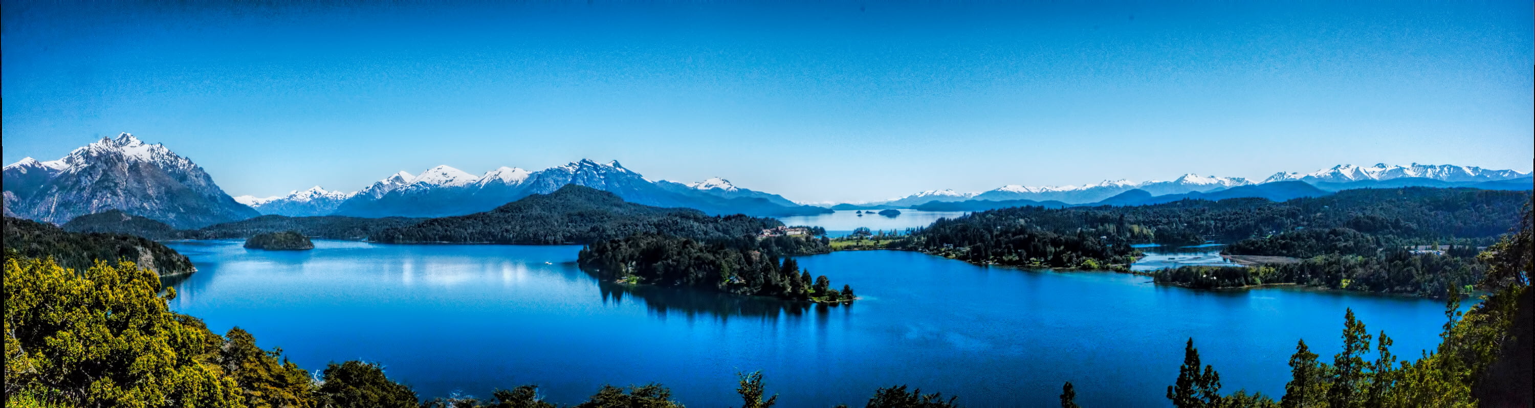 panoramic photography of body water surrounded by trees and snowy mountains under clear blue sky during daytime 2k