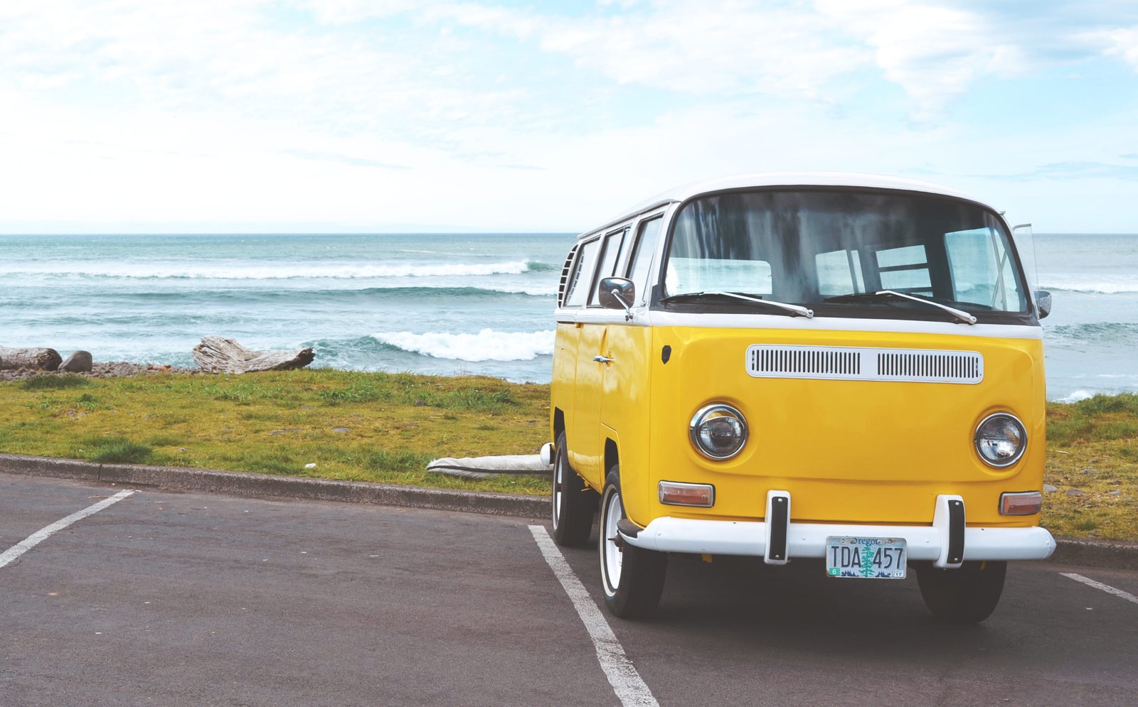 yellow Volkswagen van on concrete road and white bus parked near sea shore under cloudy sky 2k