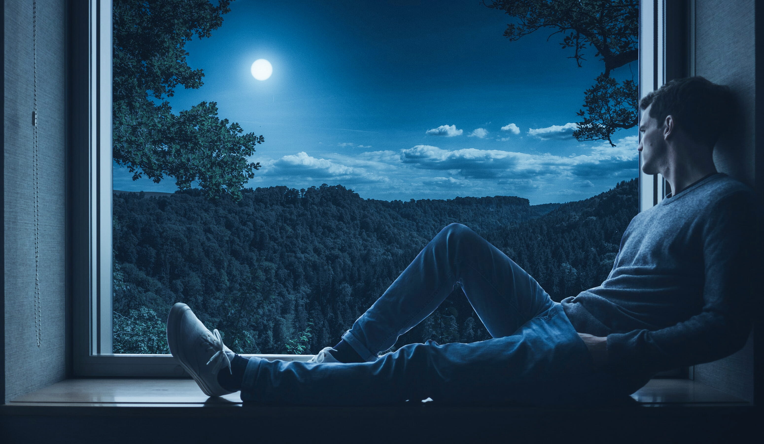 Man sitting on a window sill looking out at night person solo 2k