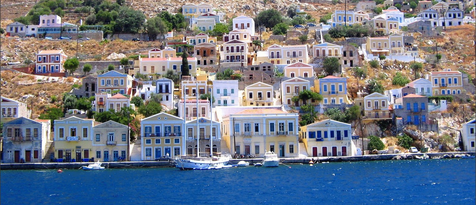 town by body of water with boat photo during daytime symi greece 2k