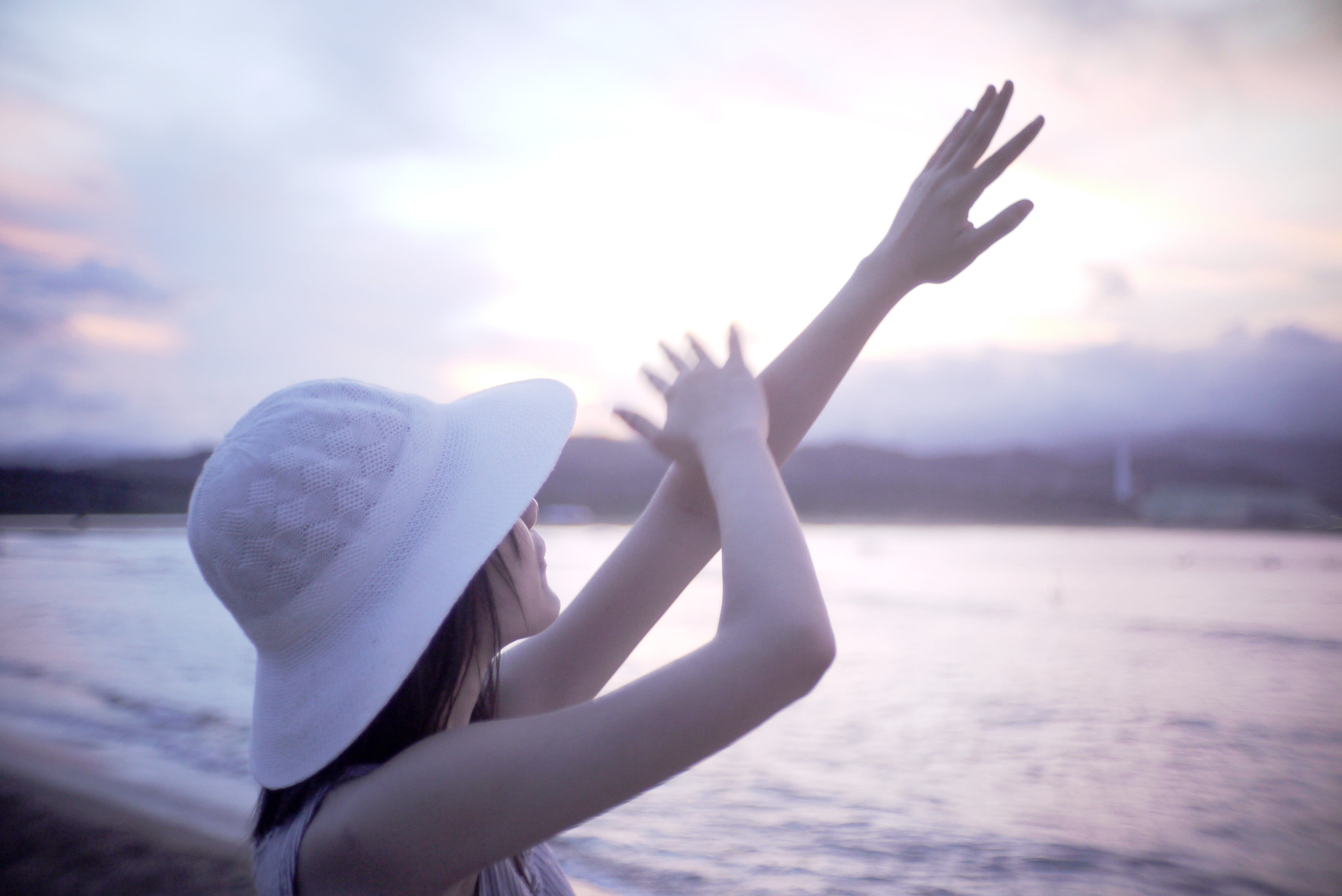 woman in white hat raising hands front of beach panasonic 2k 4k