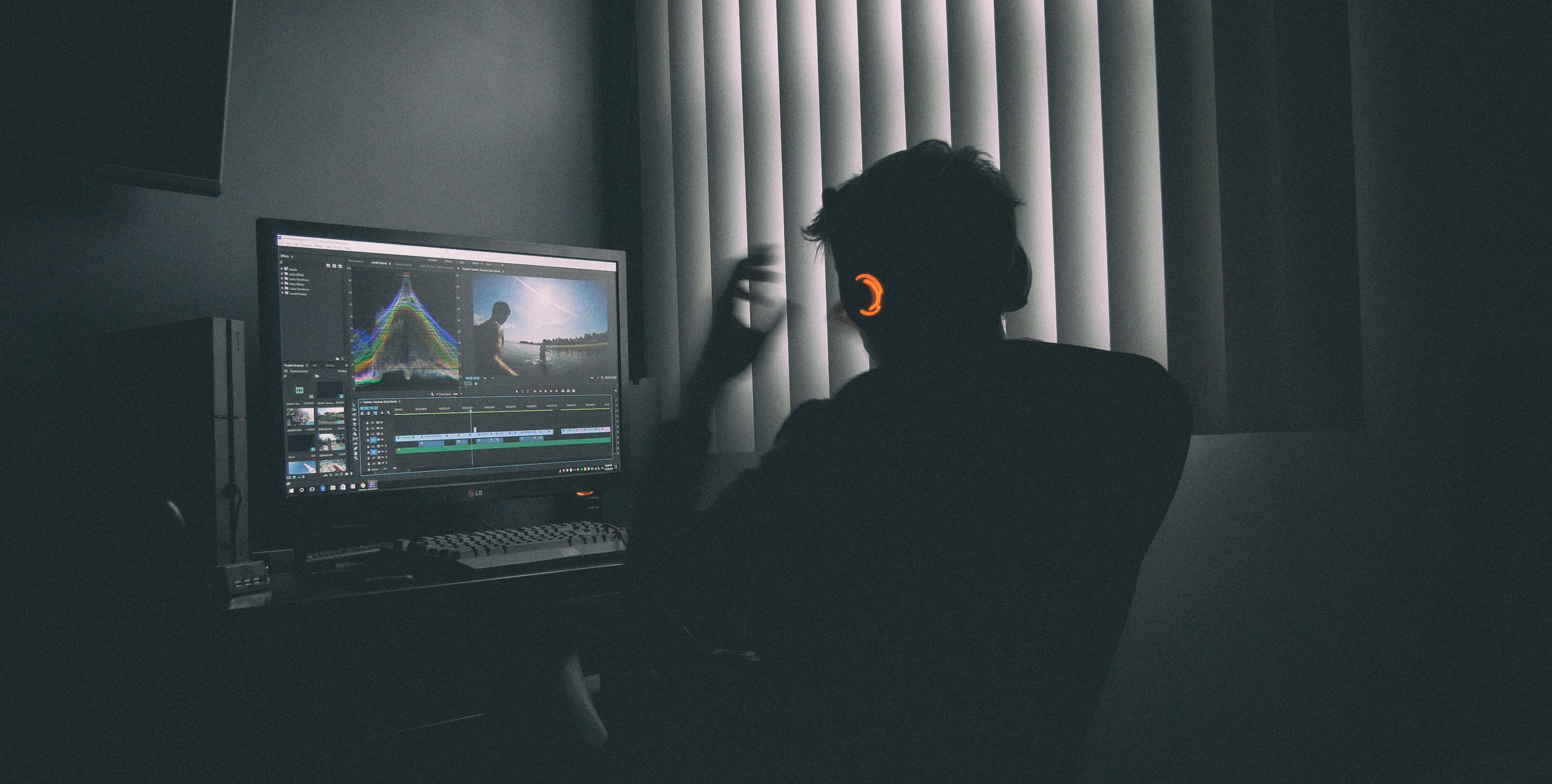shallow focus photography of man listing to music in front the computer person sitting on chair while looking monitor beside window with blinds during daytime 2k 4k
