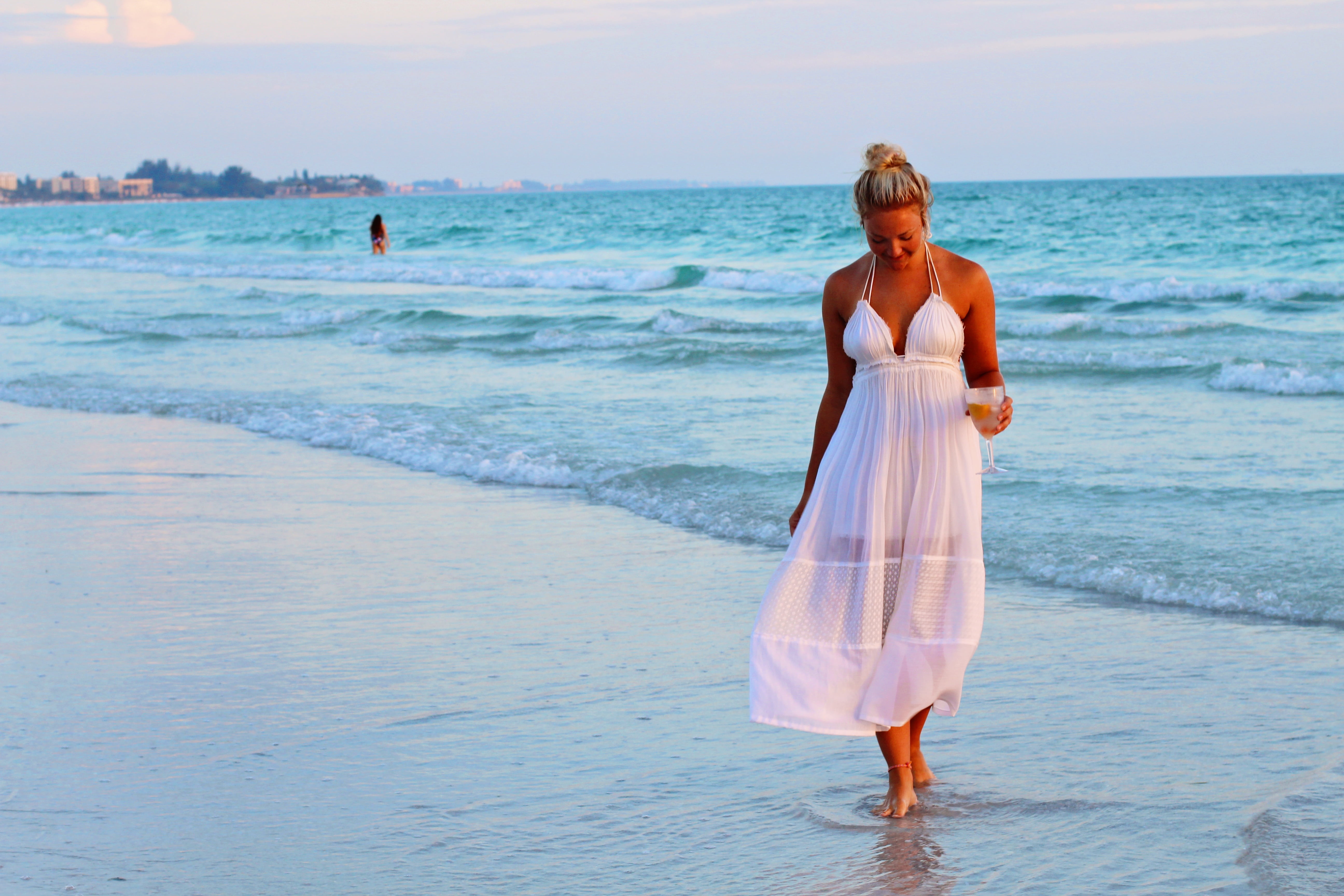 woman in white halter strap dress walking on seashore during daytime 2k 4k 5k