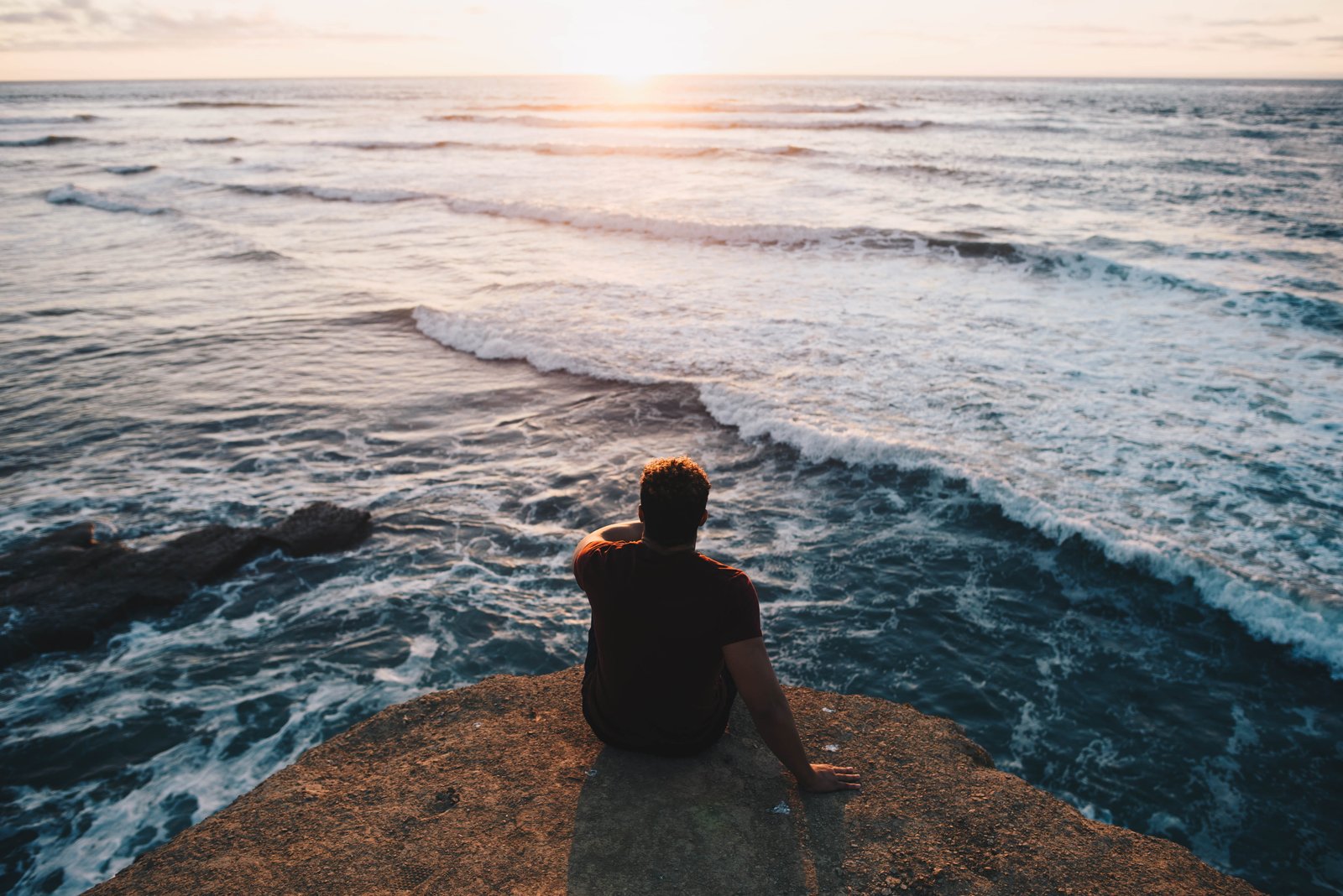 person sitting on cliff facing body of water man rock near sea 2k 4k 5k
