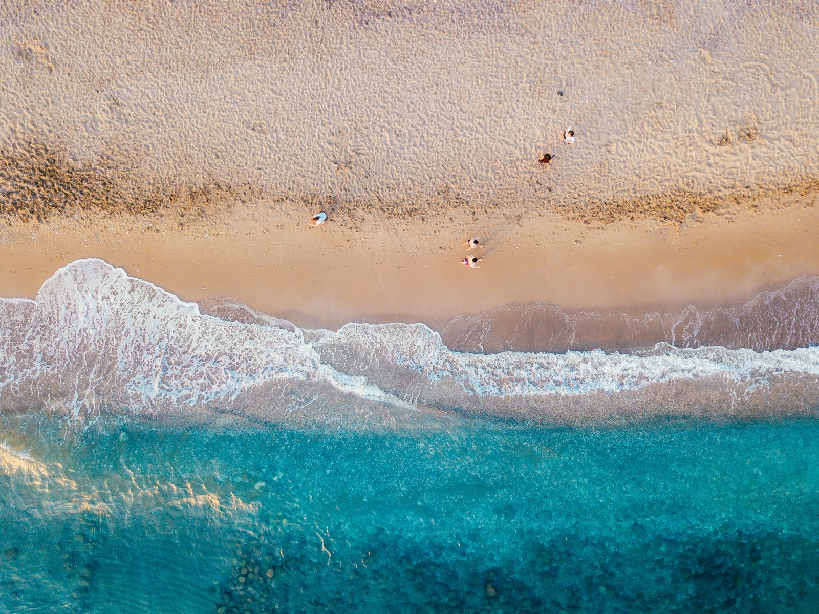 aerial photo of people standing on sand beach near teal sea wave at daytime walking during 2k 4k