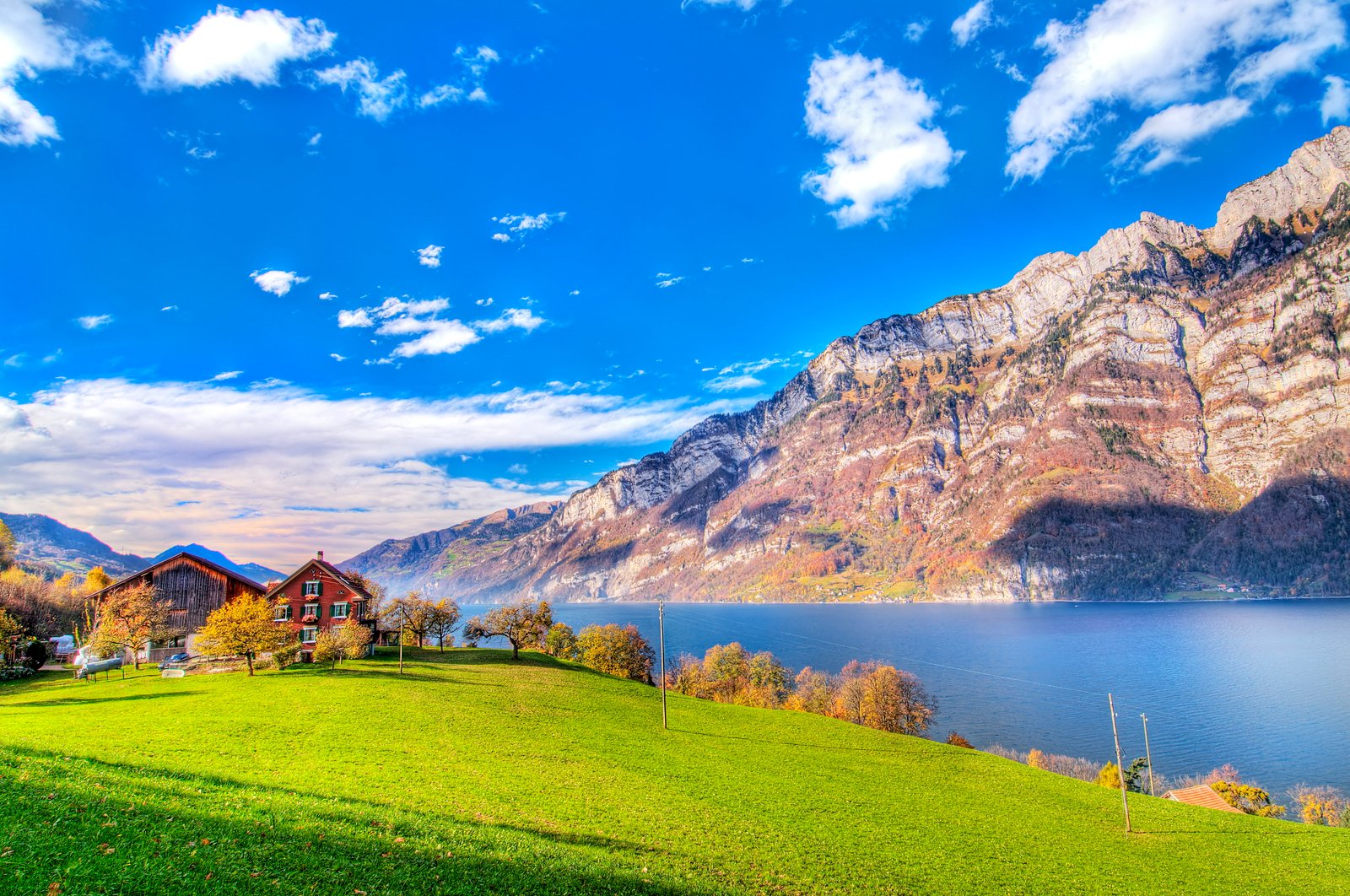 brown painted house with green grass field near calm body of water mountain as background under the blue sky 2k 4k