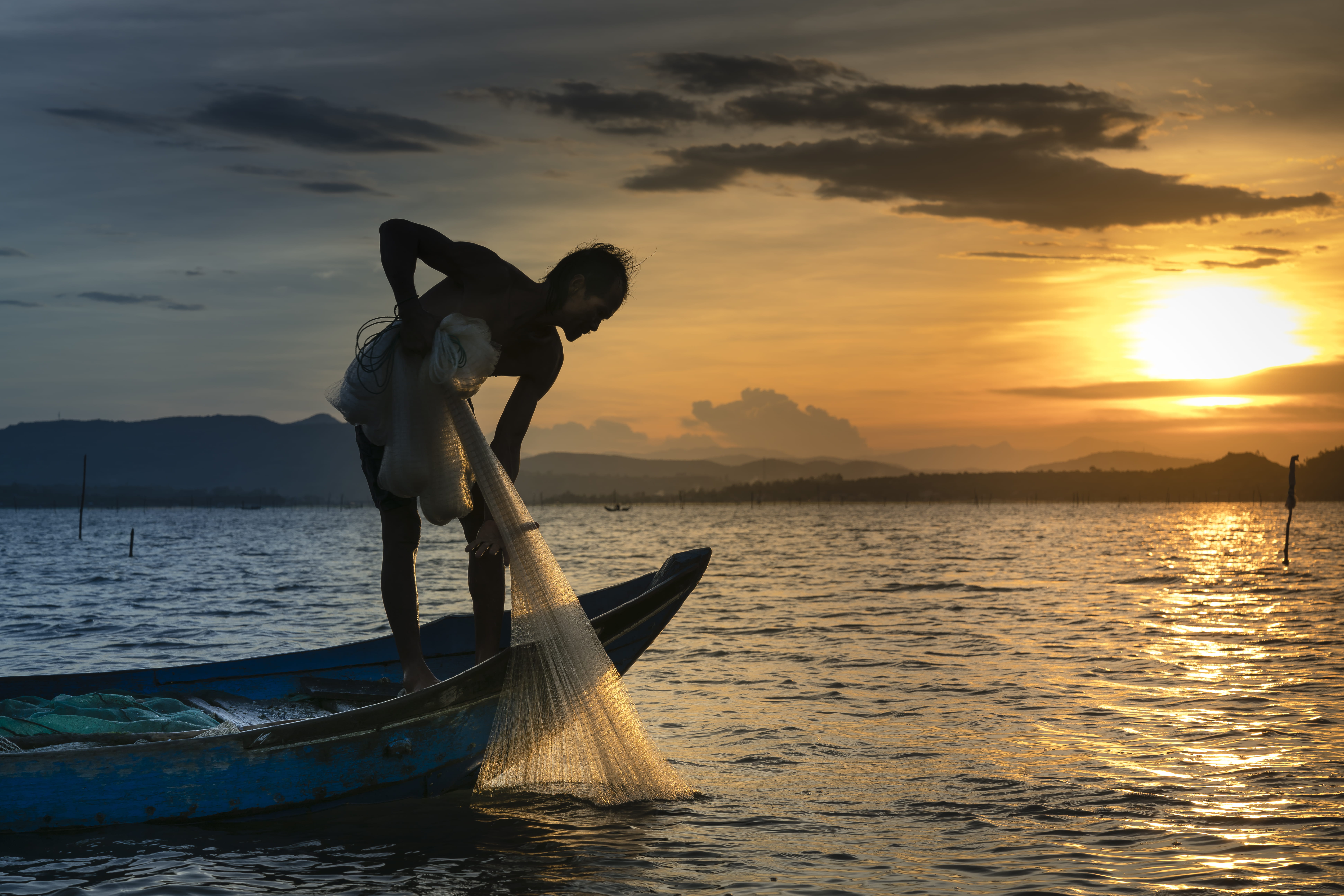 Man on Boat Holding White Mesh Fishing Net backlit beach clouds 2k 4k 5k 8k
