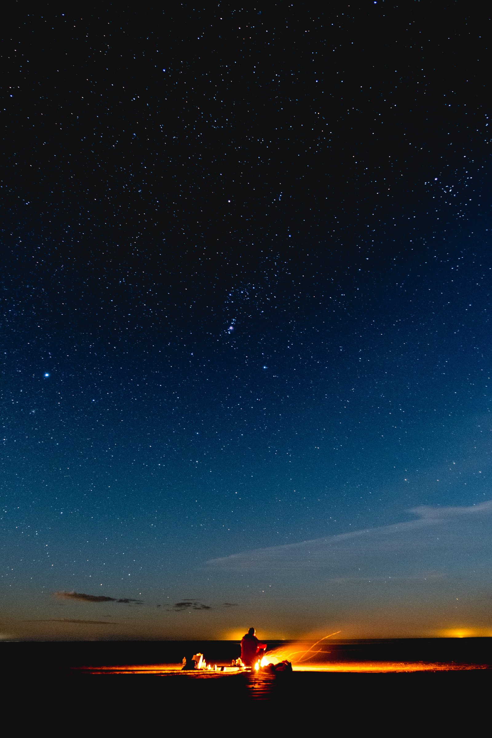 person sitting under starry night sky beach camp fire heat 2k 4k