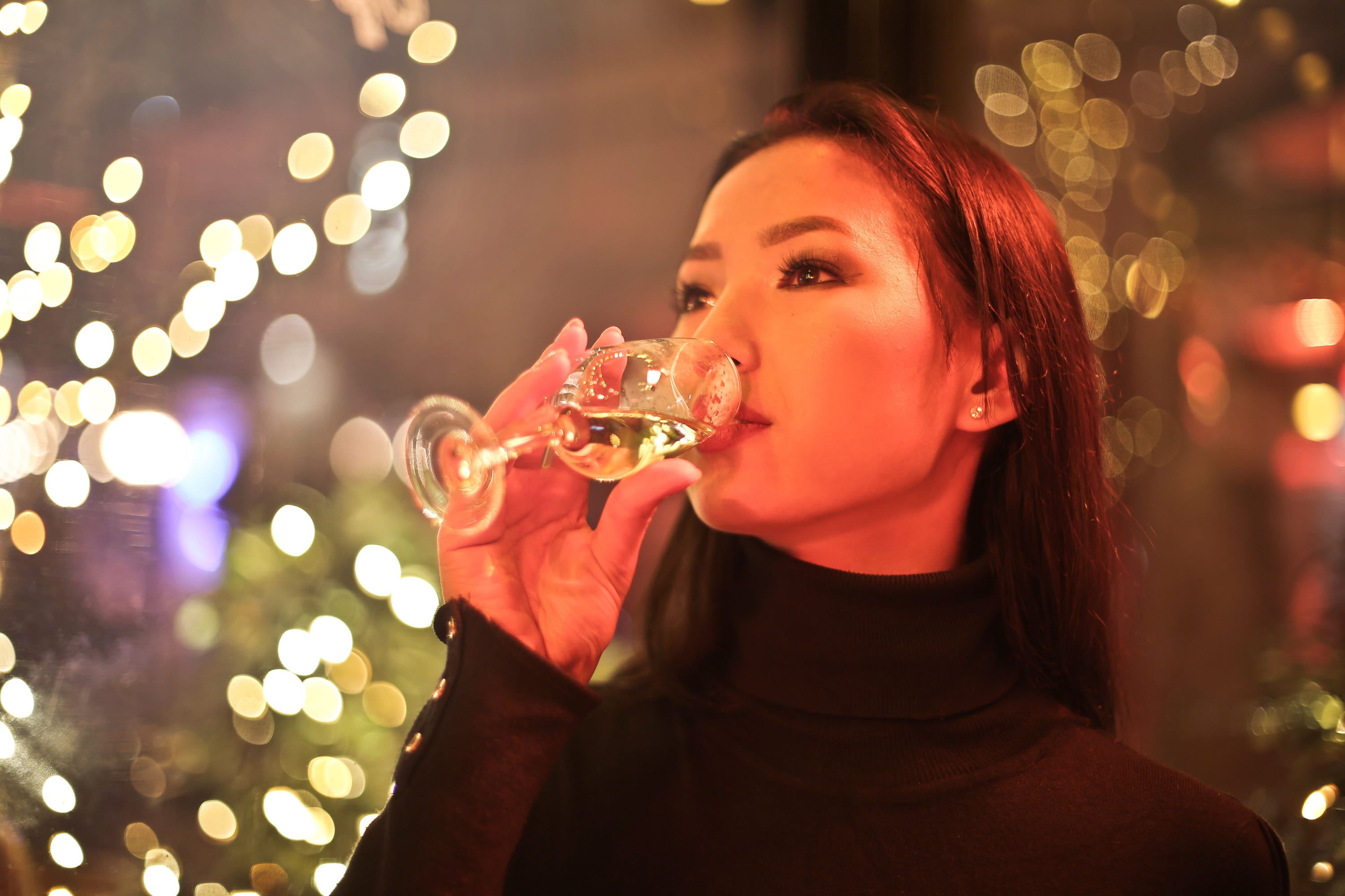 Young Adult Woman Drinking Wine in a bar with xmas bokeh lights around her 2k