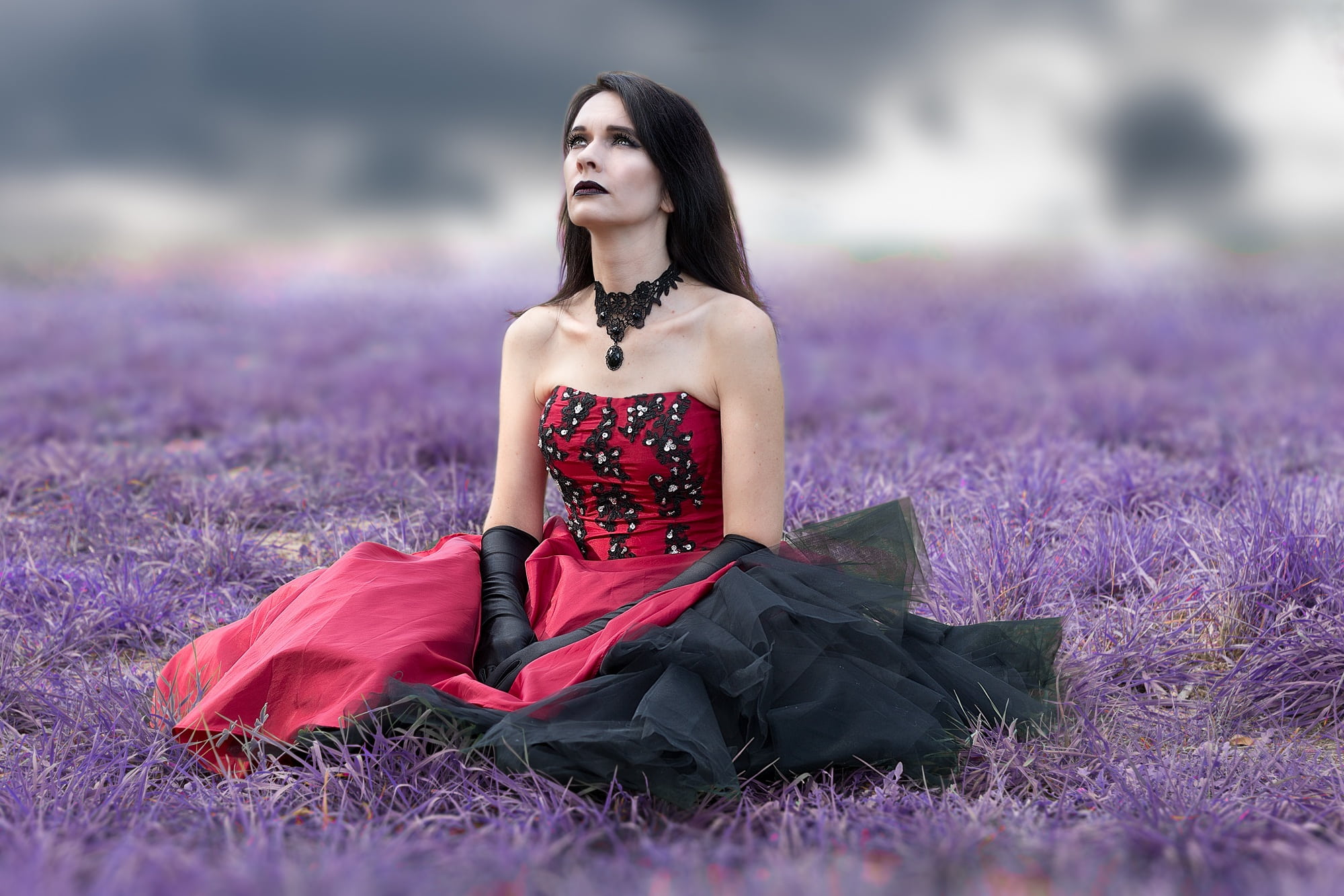 woman wearing red and black strapless dress sits on purple grass field at daytime 2k